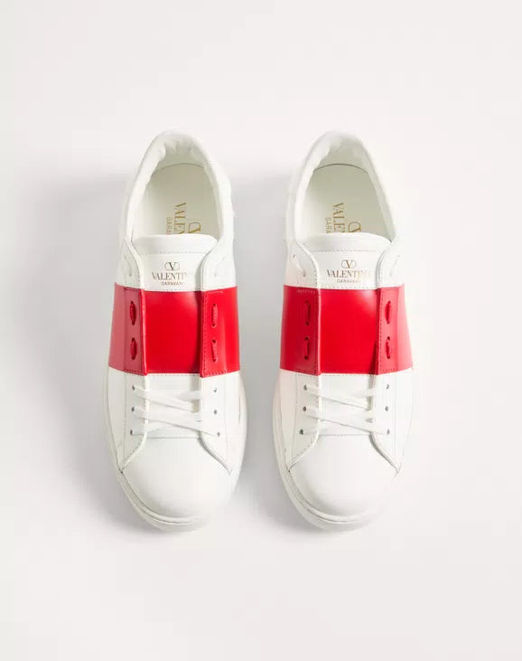 White open sneakers with red heel panels and white laces; Valentino branding on tongue.