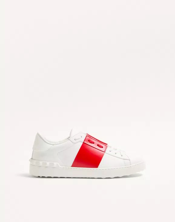 White open sneaker with red center panel and lace-up; studded rubber sole.