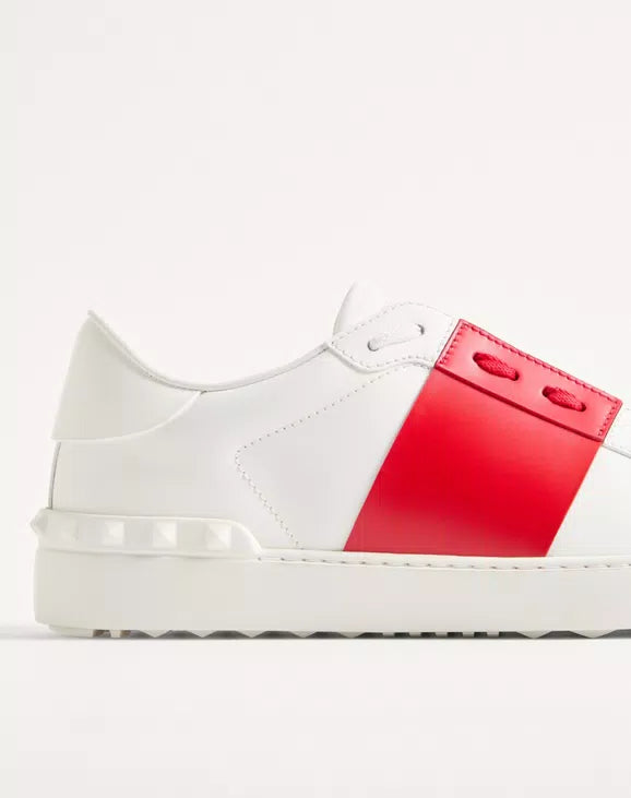 White open sneaker side profile with red strap panel and visible stitching.