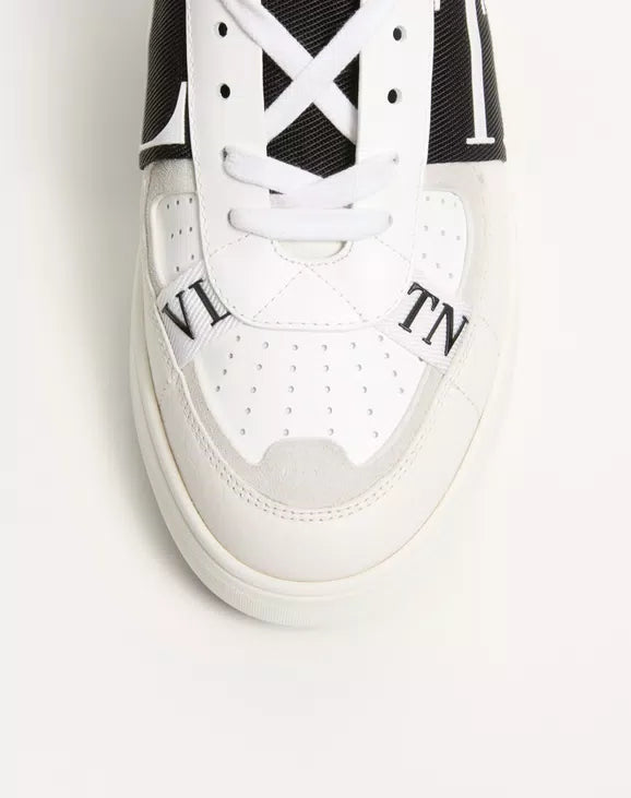 White low-top sneaker close-up with white laces, perforations, and black side trim