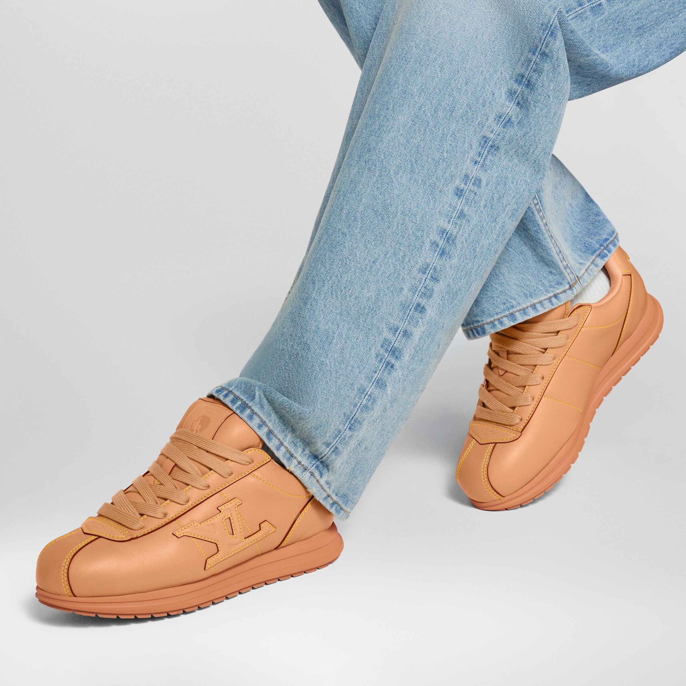 Tan lace-up LV Buttersoft sneakers on foot with light-wash blue jeans