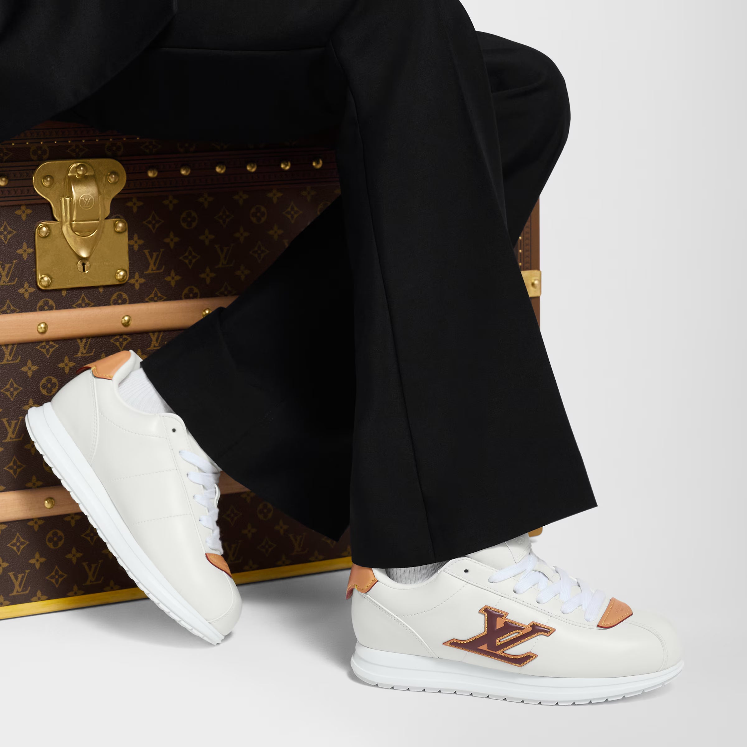 Pair of white LV Buttersoft sneakers with orange LV logo and orange heel trim, worn