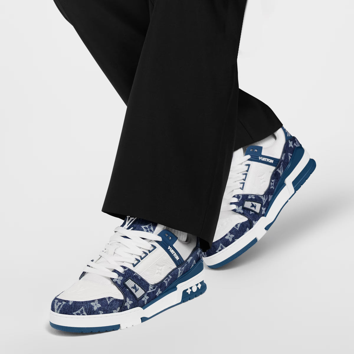 LV trainers on feet with black trousers, blue-and-white monogram design and white laces.