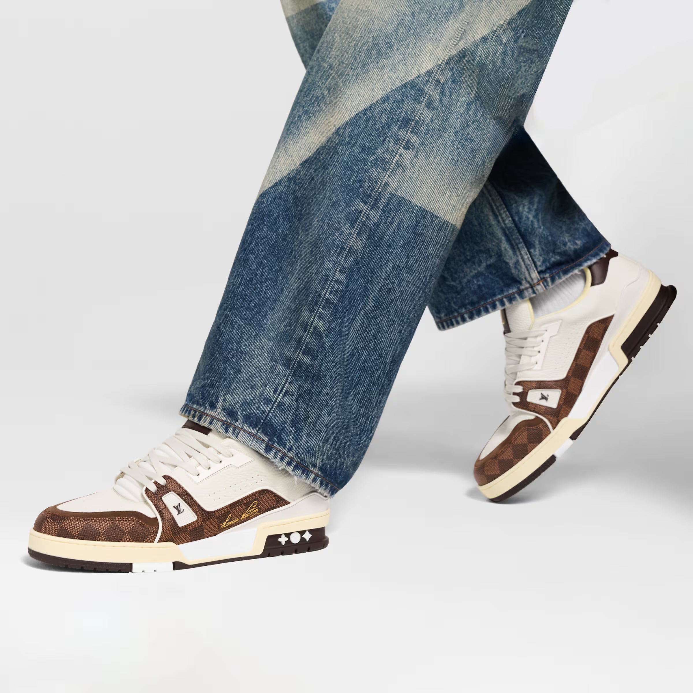 White and brown LV sneakers on feet with blue jeans, white laces and logo side.